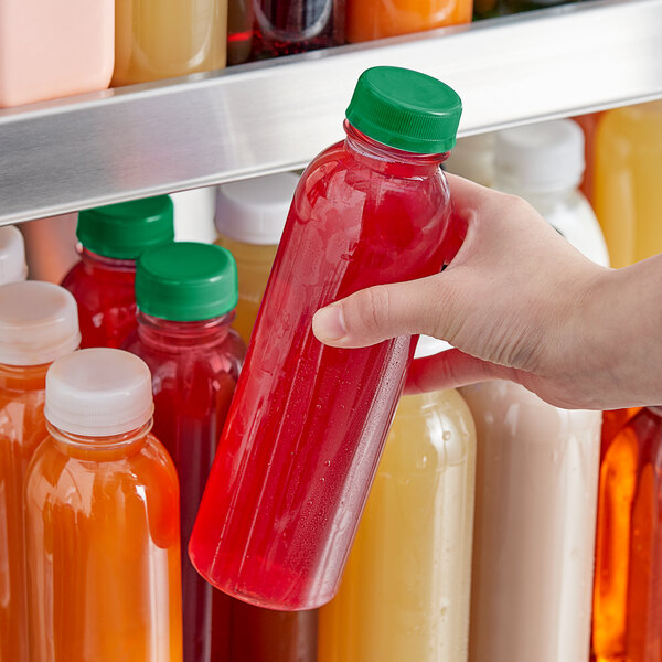 A hand holding a round clear PET juice bottle with dark green lid.