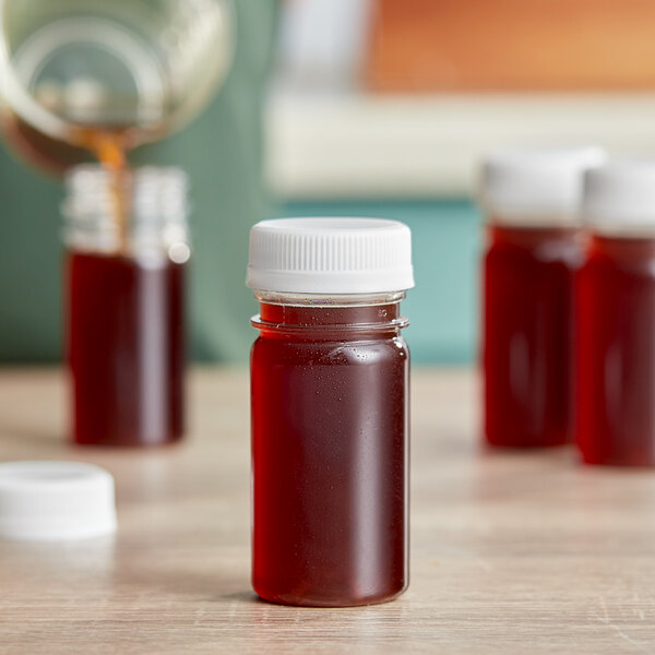 A 2.5 oz. round clear PET bottle with a white circular lid filled with brown liquid.