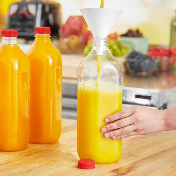 A hand pouring orange juice into a bottle of orange juice with a red cap.