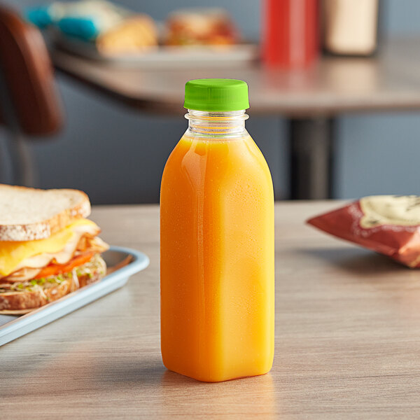 A 16 oz. Square Milkman PET Clear juice bottle with a lime green lid on a table next to a sandwich.