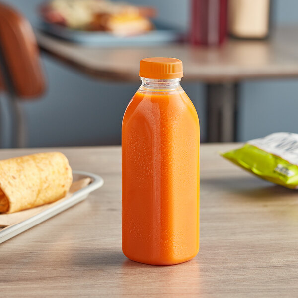 A 16 oz. Square Milkman PET clear juice bottle with an orange lid on a table.