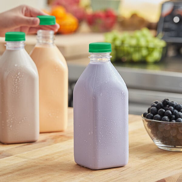A woman holding a 32 oz. clear square juice bottle with a green lid.