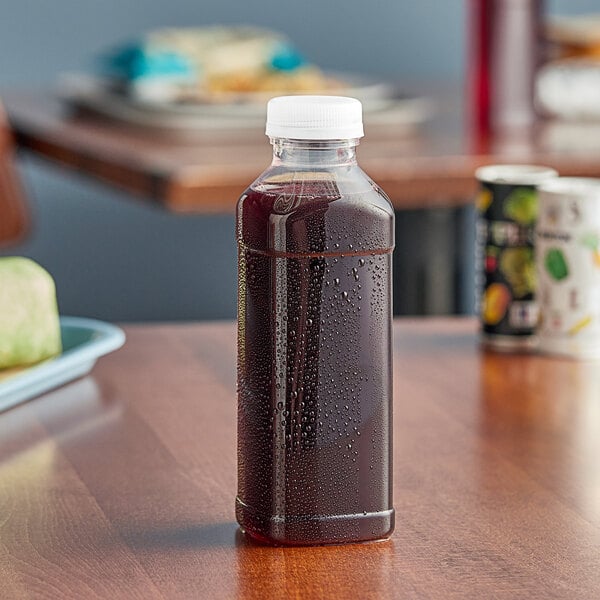 A 15.2 oz. Square PET clear juice bottle with clear liquid sitting on a table.