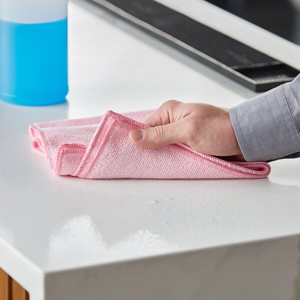 A hand wiping a counter with a red Lavex microfiber cloth.