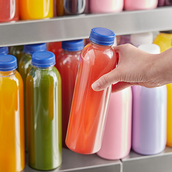 A hand holding a 16 oz. round clear juice bottle with yellow liquid and a blue lid.