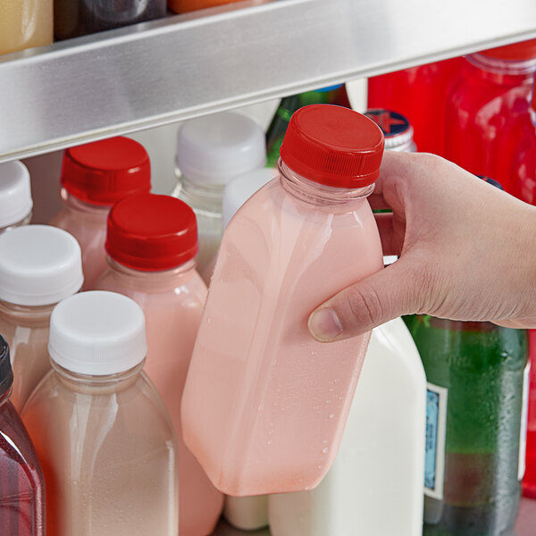 A person holding a 12 oz. Square Clear PET Milkman Juice Bottle with a red lid filled with pink liquid.