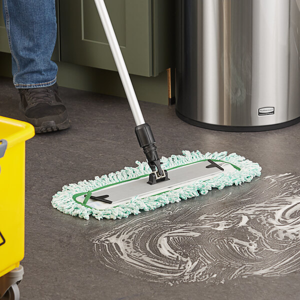 A person using a black-handled Lavex dry mop pad to clean a floor in a professional kitchen.