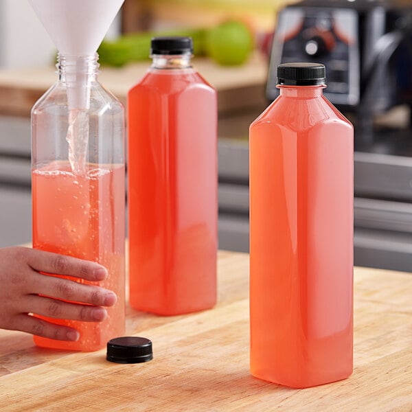 A hand pouring pink liquid into an orange 32 oz. tall square PET juice bottle.