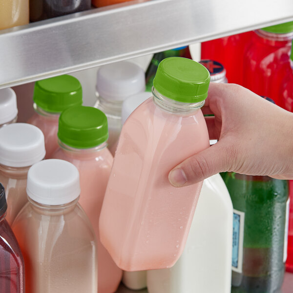 A person holding a 12 oz. square clear plastic bottle of pink juice with a lime green lid.