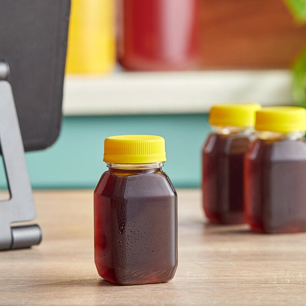 A table with 4 oz. Square PET clear energy bottles with yellow lids full of liquid on it.