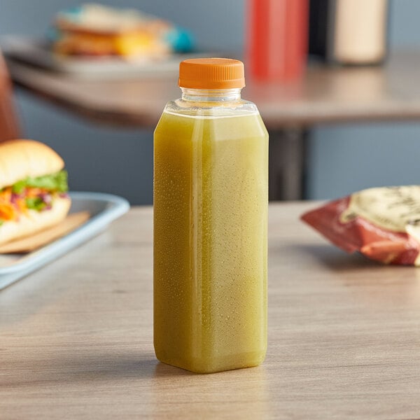 A 16 oz. tall square clear juice bottle filled with yellow liquid on a table.