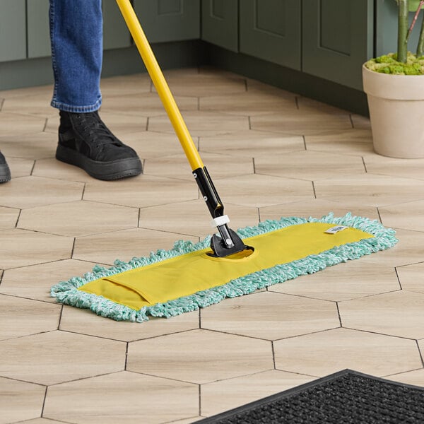 A person using a Lavex 24" microfiber dust mop with a yellow handle on a tile floor.