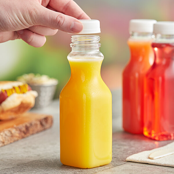 A hand holding a square PET clear carafe juice bottle filled with orange juice.