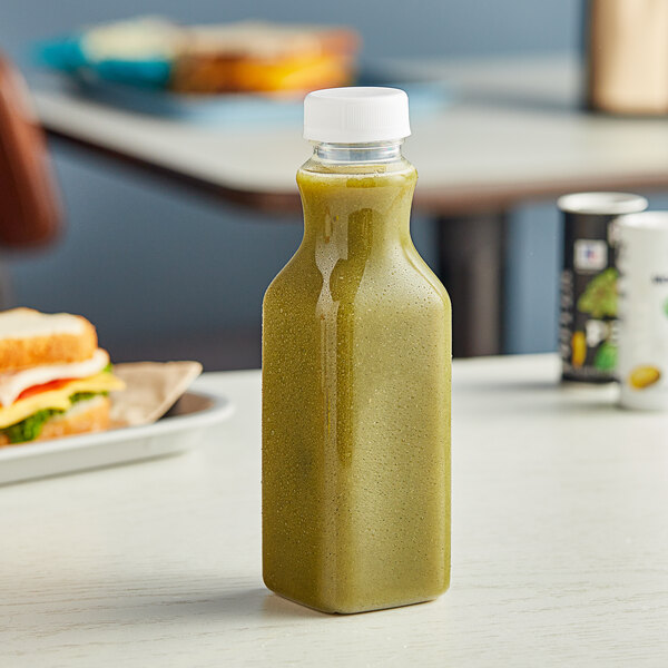 A Square PET clear carafe juice bottle filled with green liquid on a table.