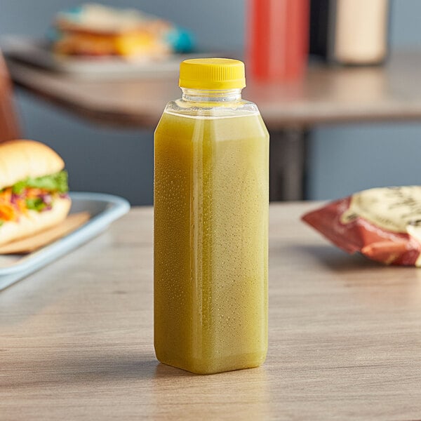 A 16 oz. tall square PET clear juice bottle with yellow liquid on a table.