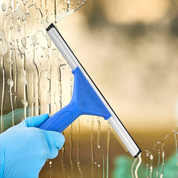 A gloved hand using an Ettore 10" All-Purpose Squeegee to clean a window.