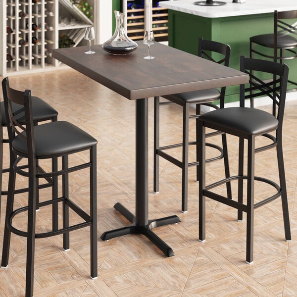 A Lancaster Table & Seating rectangular bar height table with a vase, a glass, and a decanter on it.