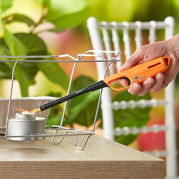 A hand holding a Scripto Torch Flame Max Multi-Purpose Lighter in an outdoor catering setup.