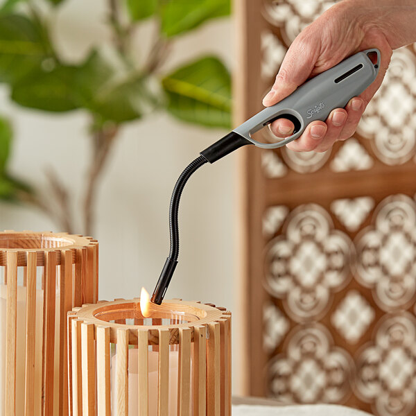 A hand using a Scripto Aim 'N Flame Max Flex Multi-Purpose Lighter to light wooden candles.