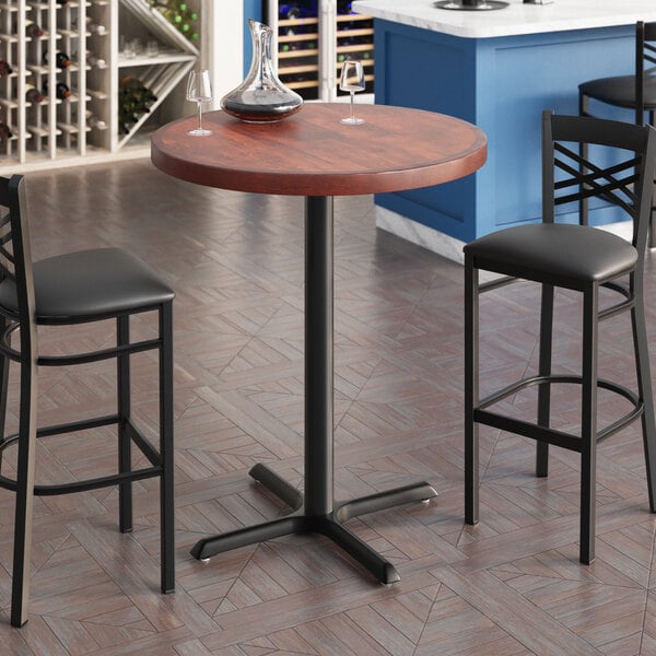 A Lancaster Table & Seating bar table with two chairs and a wine bottle on it.