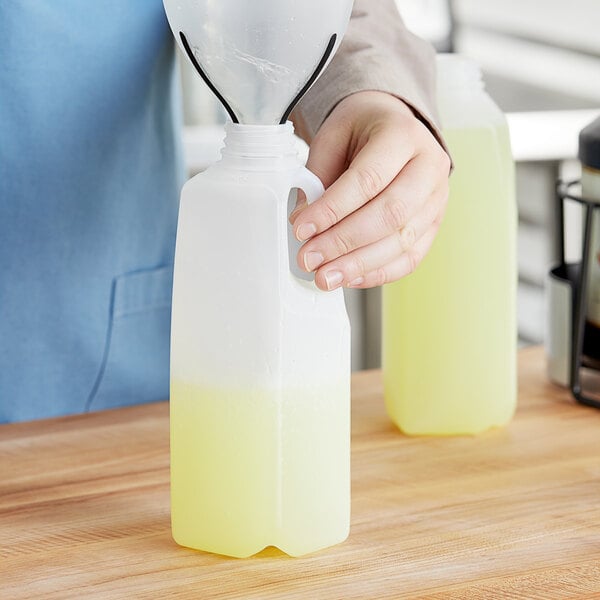 A hand pouring liquid into a translucent plastic jug with a handle.