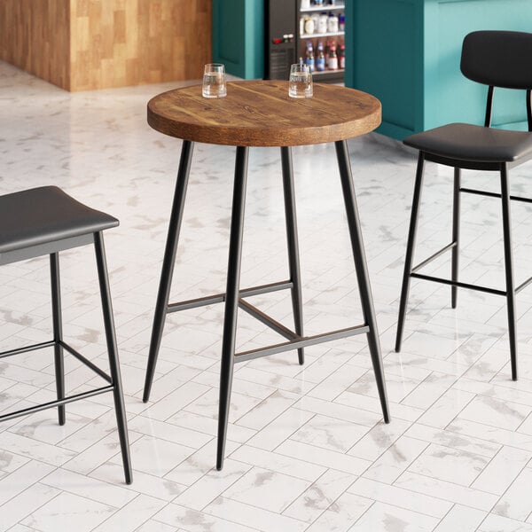 A Lancaster Table & Seating Mid-Century bar height table with a butcher block top and vintage finish, with two wooden bar stools.