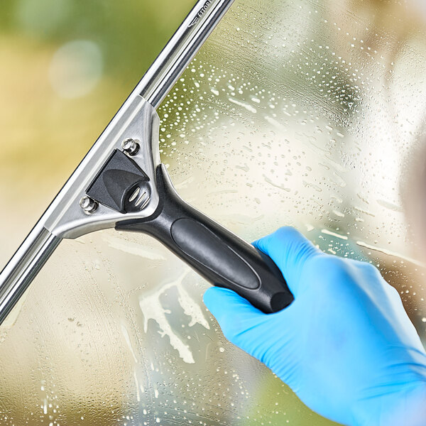 A hand in a blue glove using an Ettore Pro+ squeegee with a black handle to clean a window.