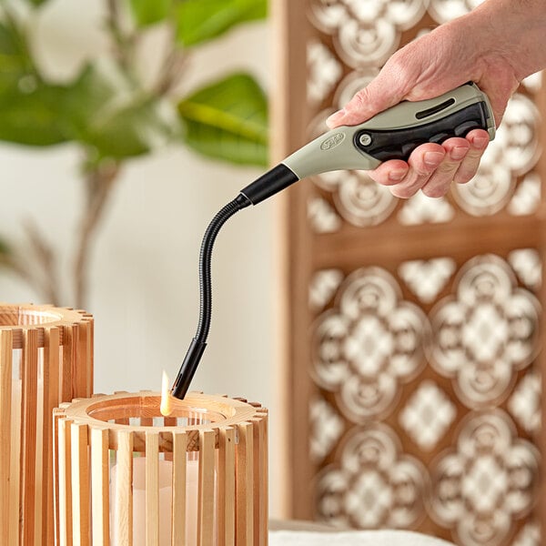 A hand using a Scripto EZ-Squeeze Flex refillable multi-purpose lighter to light a wood candle holder.