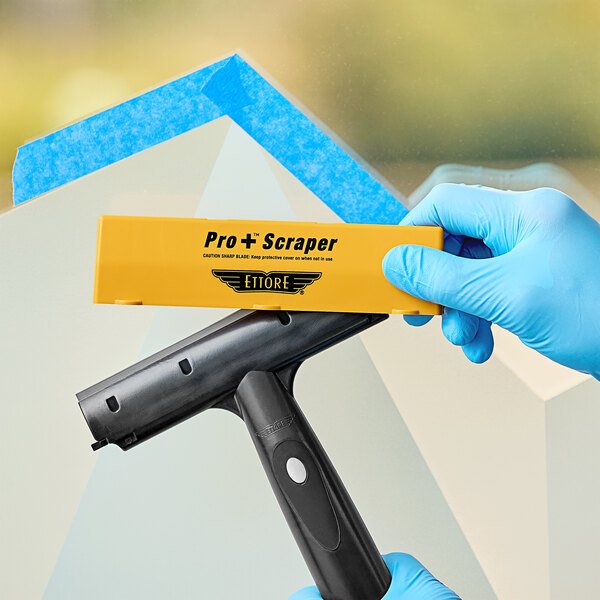 A hand in a blue glove holding a yellow and black Ettore Pro+ Contour scraper blade cover.