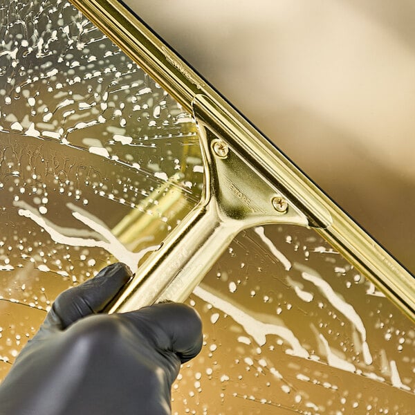 A hand wearing black gloves using an Ettore brass squeegee handle to clean a window.