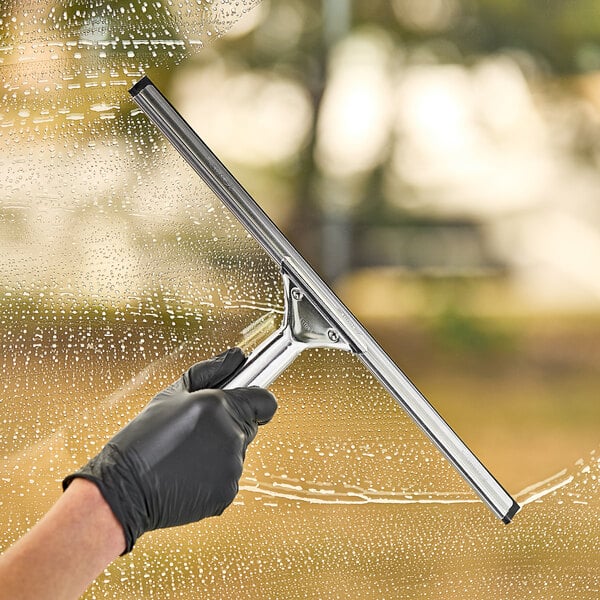 A hand with a black glove using an Ettore stainless steel squeegee to clean a window.