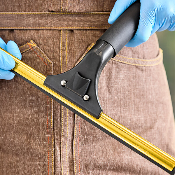 A person wearing blue gloves using an Ettore brass squeegee with a foam grip.