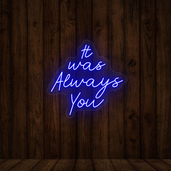 A blue "It Was Always You" Crazy Neon LED sign on a wood wall.