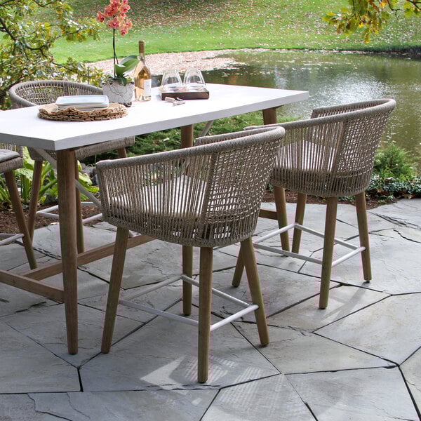 An Outdoor Interiors wheat rope and antique wash eucalyptus counter height chair with an olefin cushion on a stone patio.