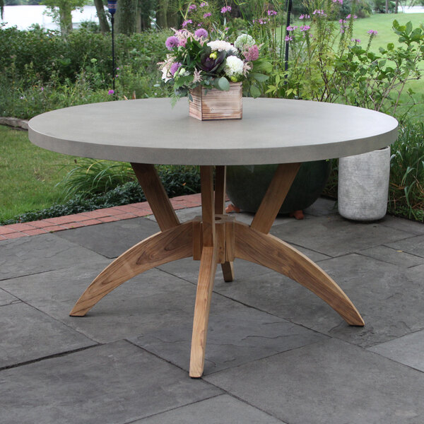 An Outdoor Interiors teak and composite dining table on a patio with a flower arrangement on it.