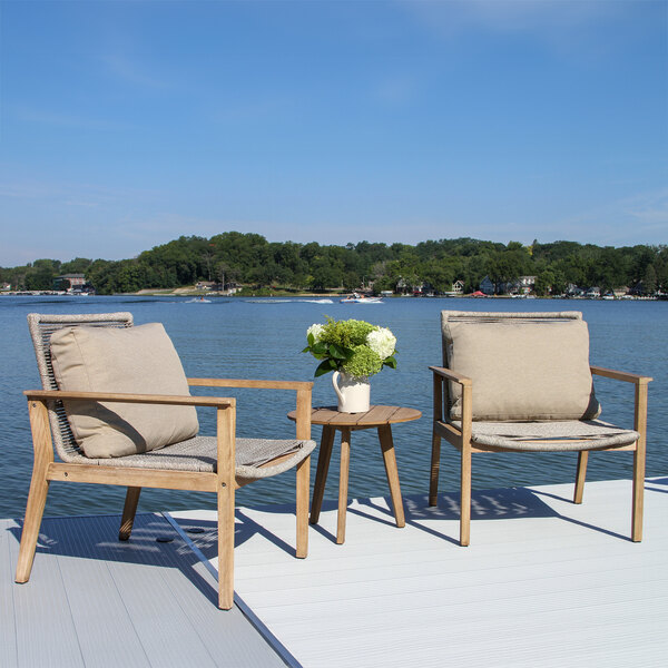 An Outdoor Interiors eucalyptus and rope lounge chair with a pillow on a dock overlooking water.
