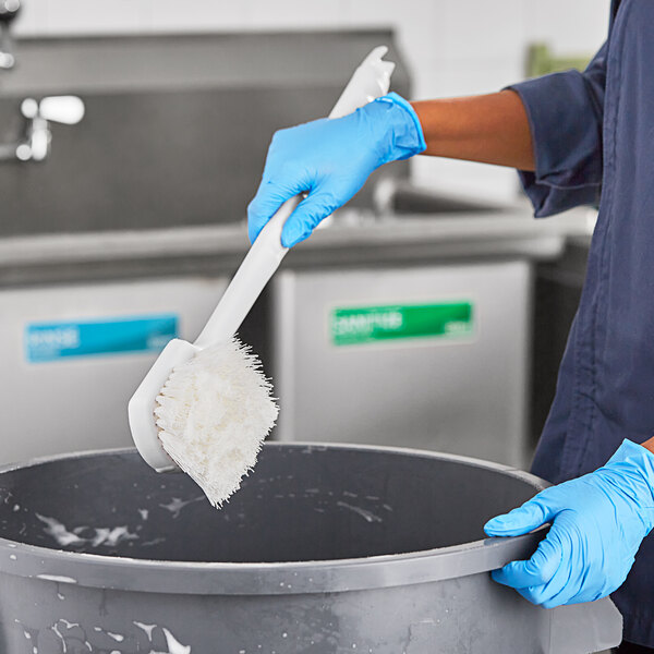 A person using a Lavex white utility brush to clean a bucket.
