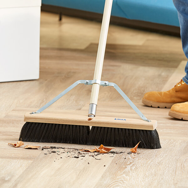 A person using a Lavex galvanized steel brace to sweep the floor with a broom.