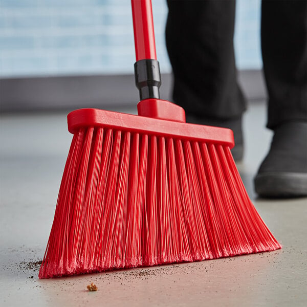 A person using a red Lavex angled broom to sweep the floor.