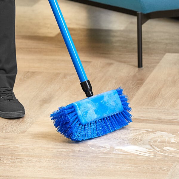 A person scrubbing a floor with a blue Lavex brush head.