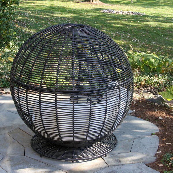 An Outdoor Interiors black wicker dome chair with a white cushion on a stone patio.