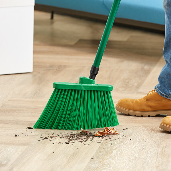 A person sweeping a wooden floor with a green Lavex broom.