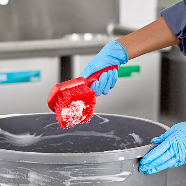 A person cleaning a large container with a Lavex red floating utility brush.