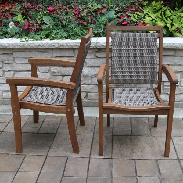 Two Outdoor Interiors Driftwood Gray Wicker and Eucalyptus stackable arm chairs on a brick patio.