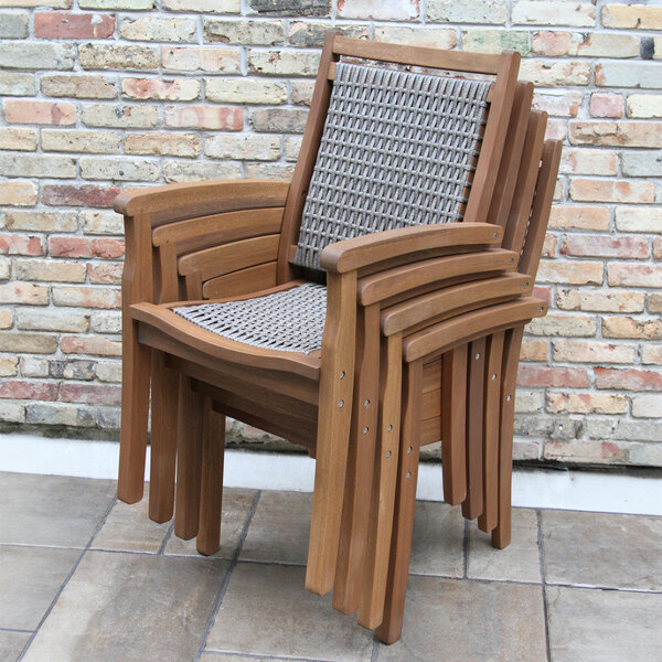 A stack of Outdoor Interiors Driftwood Gray Wicker and Eucalyptus Arm Chairs with wooden legs and woven seats.