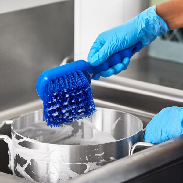 A person in blue gloves using a Lavex blue polyester utility brush to scrub a pot.
