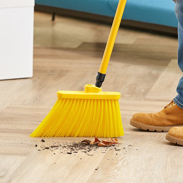 A person sweeping a wooden floor with a yellow Lavex broom.