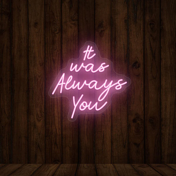 A pink Crazy Neon "It Was Always You" LED sign on a wood wall.