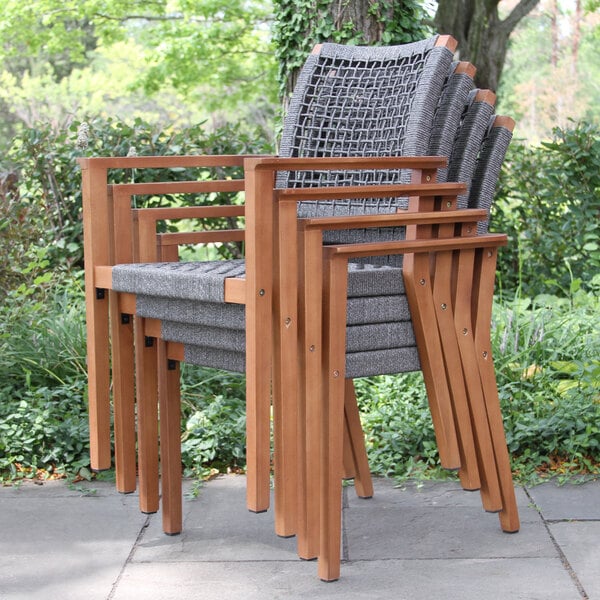 A stack of Outdoor Interiors gray rope and eucalyptus chairs outside.