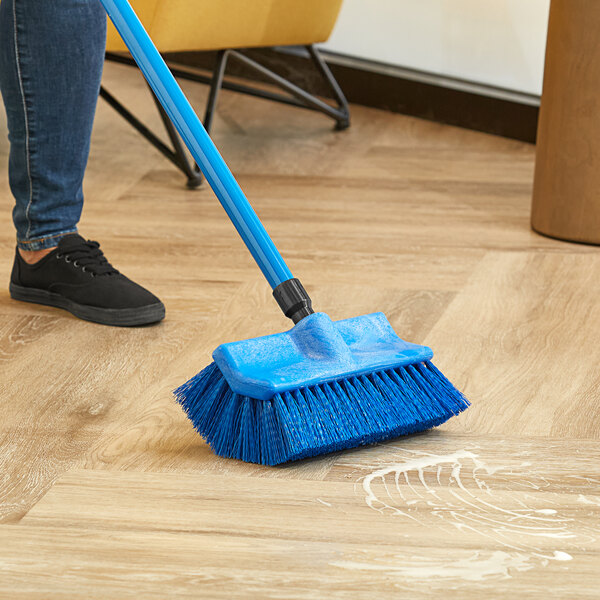A person using a Lavex blue bi-level floor scrub brush to clean a floor.